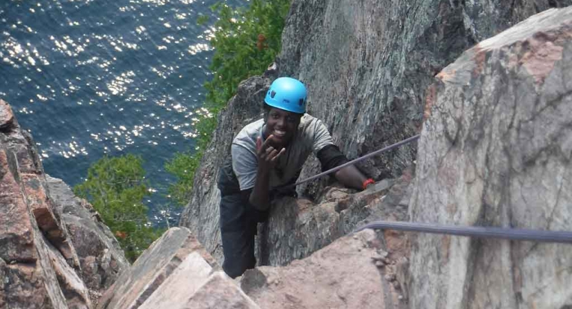 a person who is rock climbing above a body of water smiles at the camera